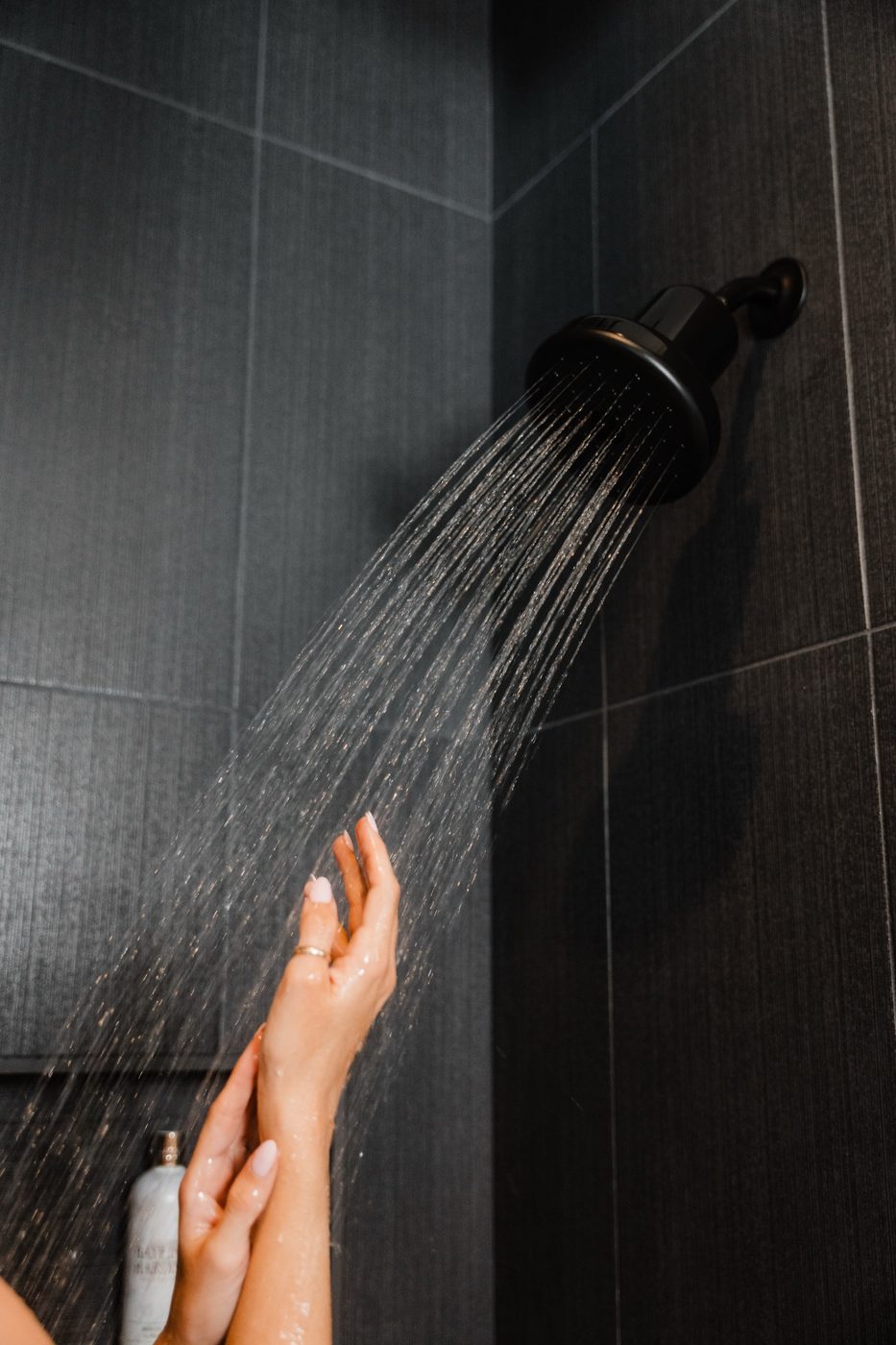 Hands in dark-tile shower spray from a Rorra Showerhead