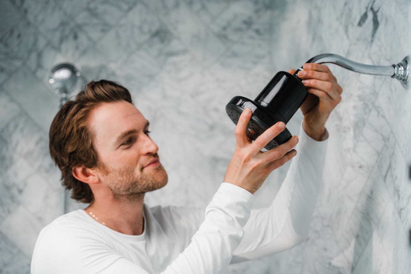 Man installing a Rorra Showerhead on white marble tile
